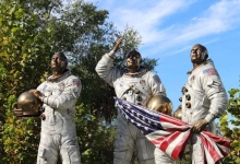 Bronze statue of Apollo astronauts at Cape Canaveral, holding a flag.