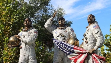 Bronze statue of Apollo astronauts at Cape Canaveral, holding a flag.