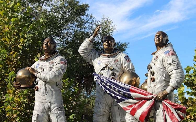 Bronze statue of Apollo astronauts at Cape Canaveral, holding a flag.